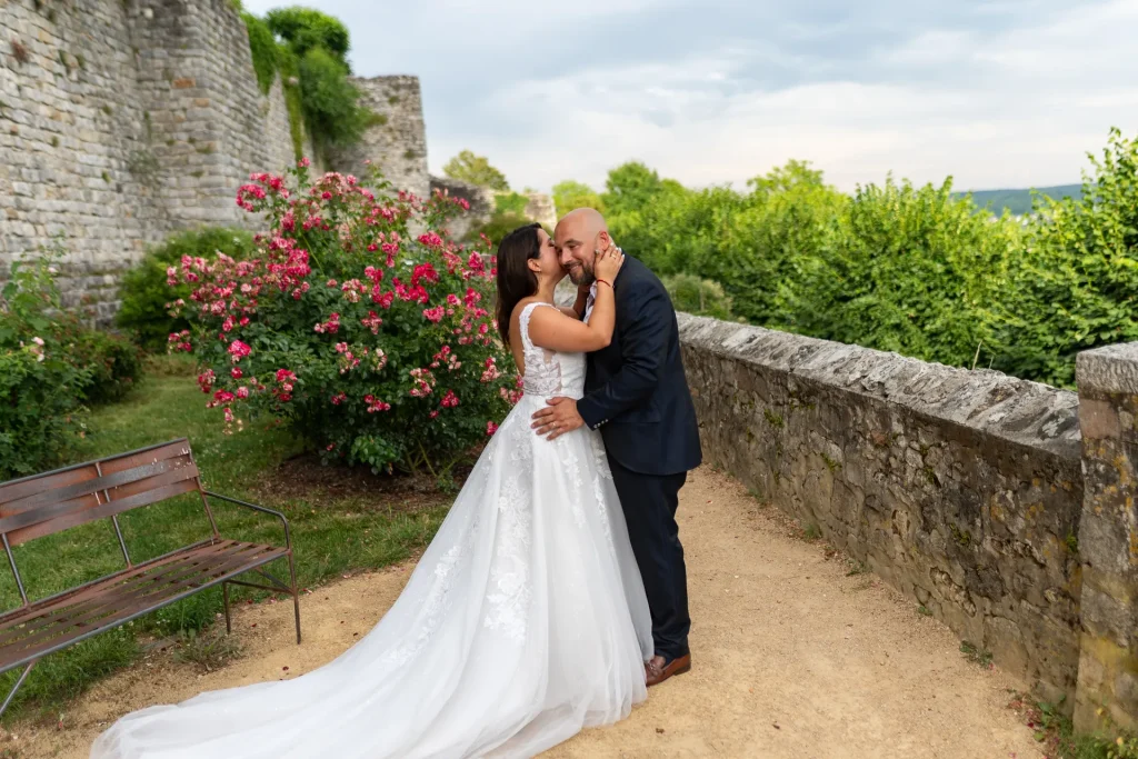 Couple de mariés s’embrassant devant un mur de pierre et des rosiers lors d’une séance photo de mariage en extérieur près de Reims