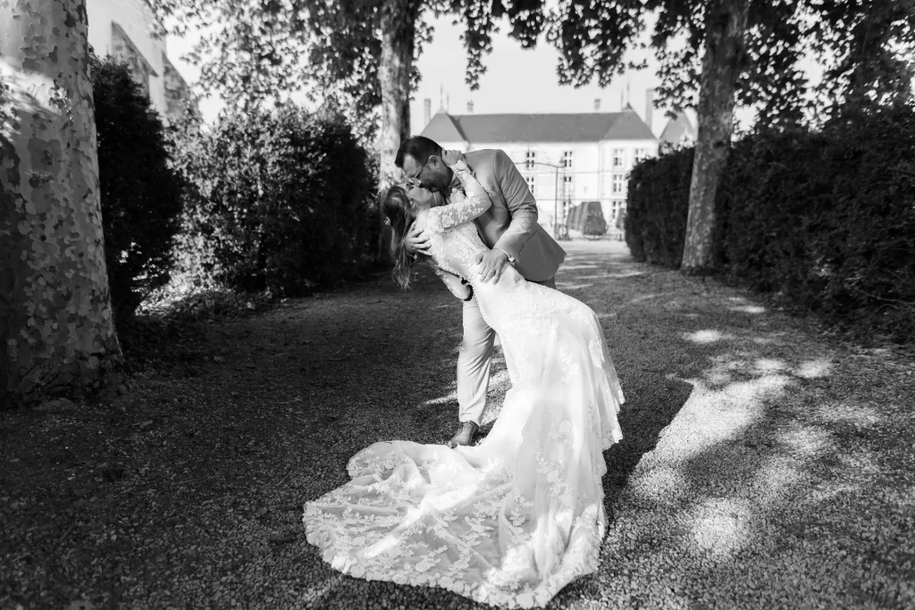 Marié penchant sa femme en arrière pour un baiser, robe de dentelle, allée du château de Vitry-la-Ville, photo noir et blanc