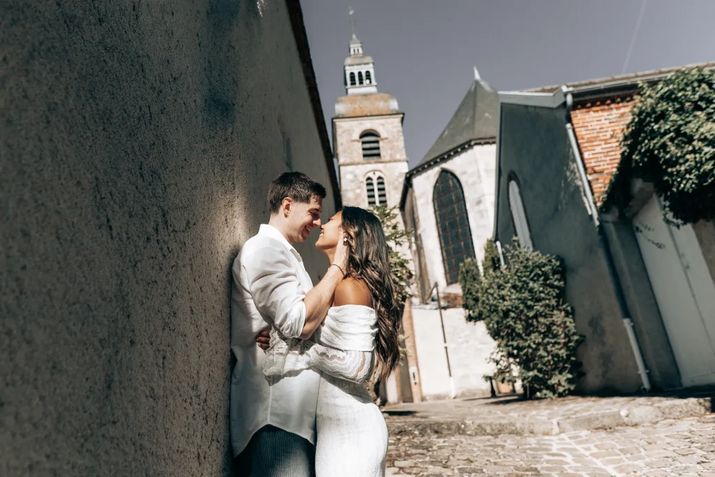Jeunes mariés complices devant une église dans une ruelle pavée